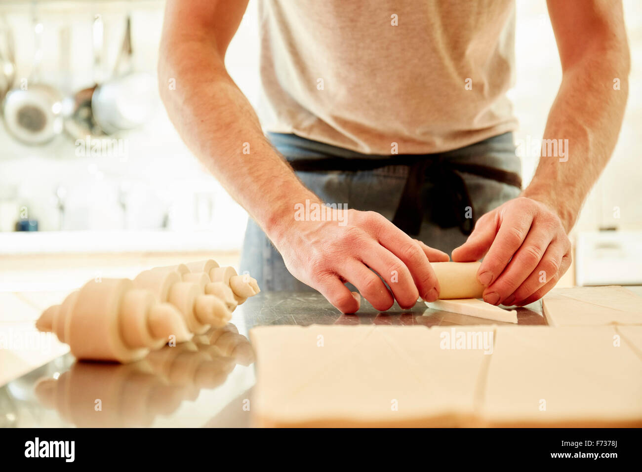 Un baker lavorando su una superficie infarinata fino al rotolamento di quadratini di pasta in croissant forme prima della cottura. Foto Stock