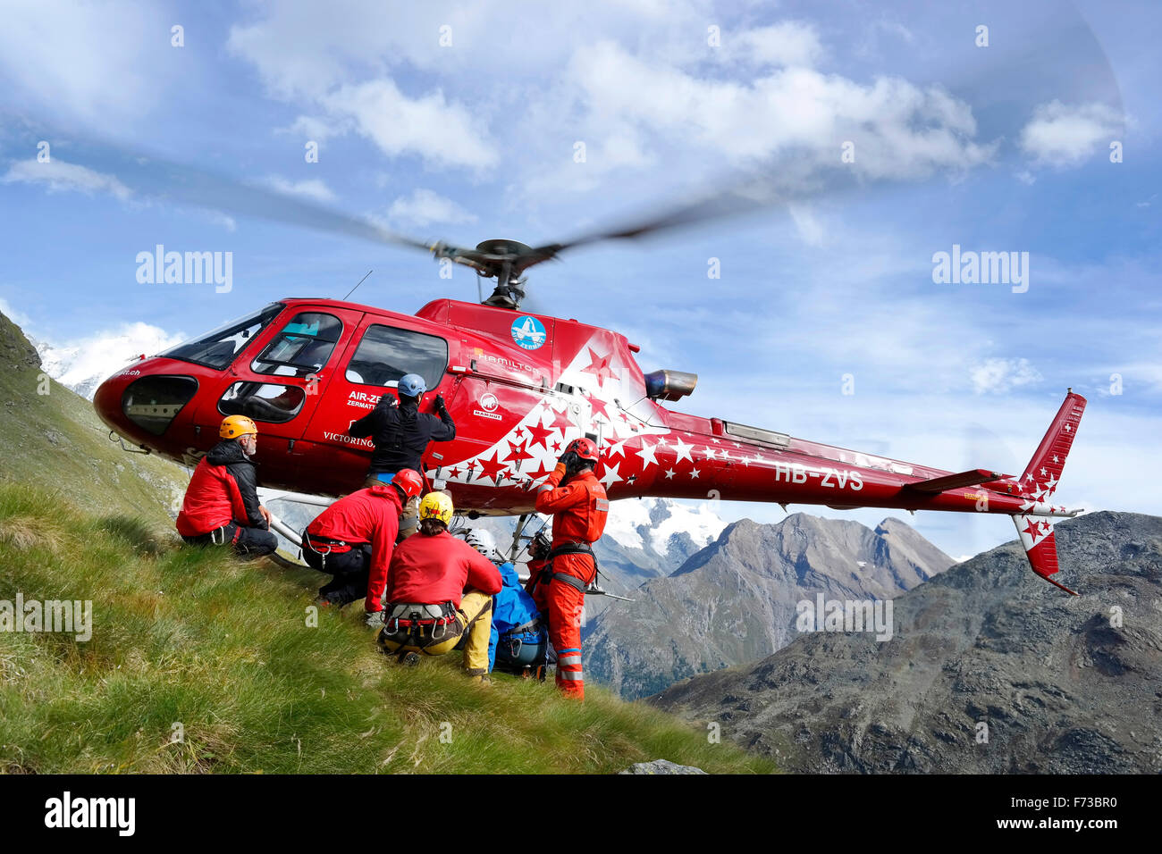 I soccorritori di montagna sono l'atterraggio di un aereo elicottero Zermatt su un pendio erboso nelle Alpi Svizzere. Foto Stock