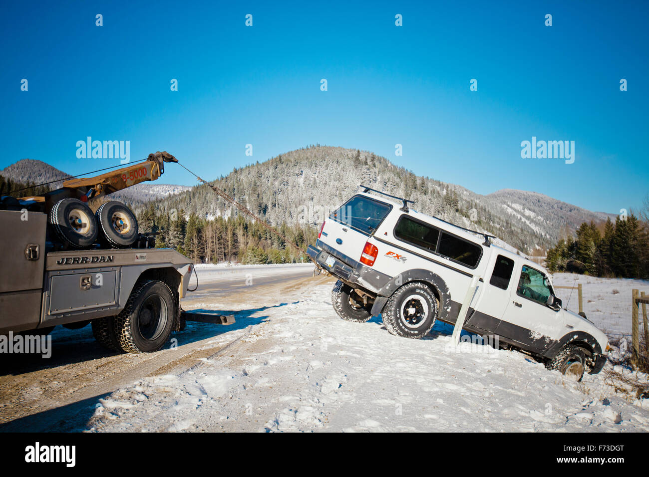 Un carrello di traino tira un mid-size carrello fuori di una neve riempito fosso. Foto Stock