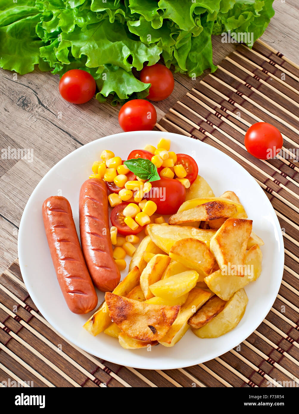 La Salsiccia con patate fritte e le verdure su una piastra Foto Stock