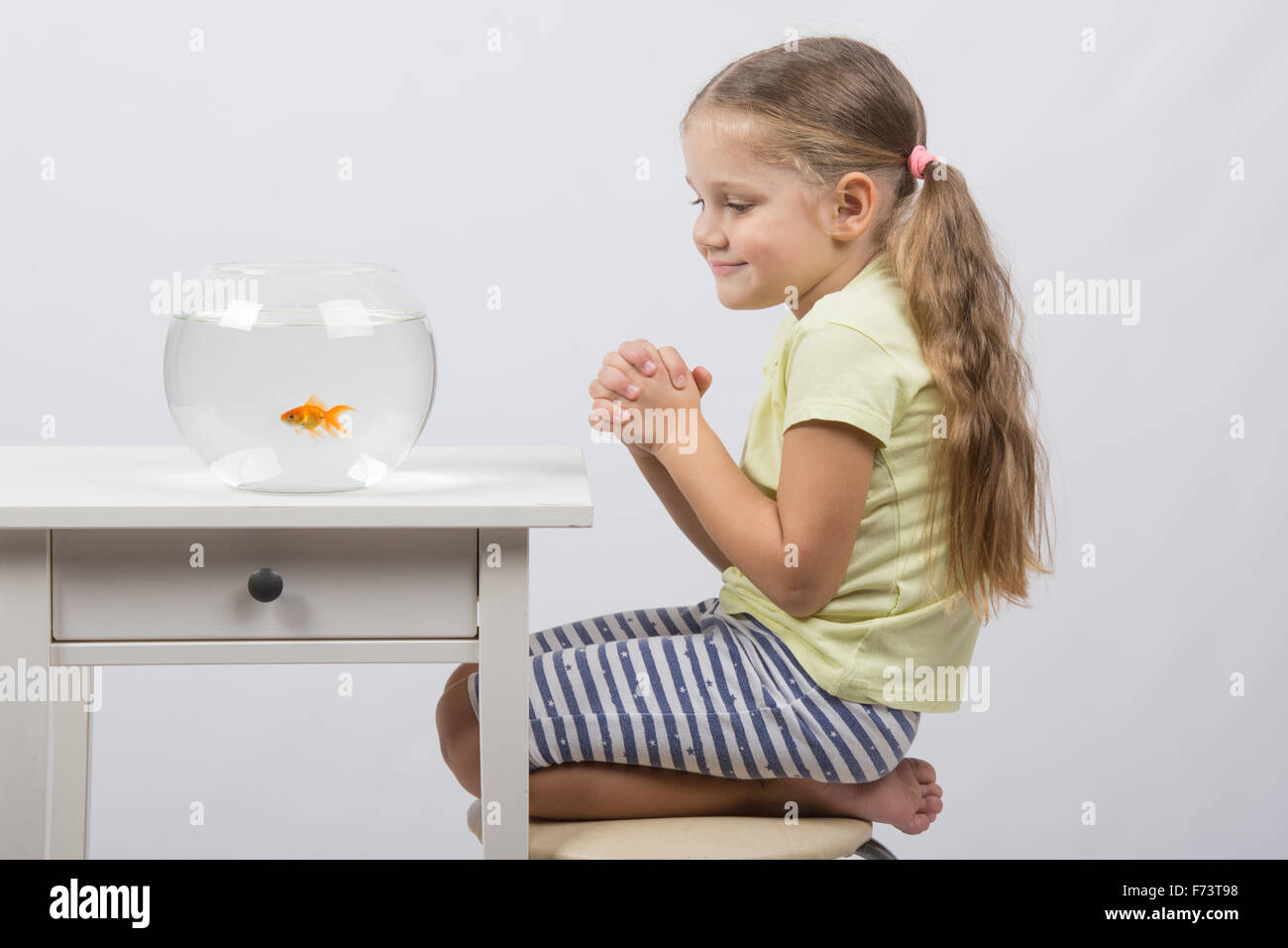 Felice di quattro anni di ragazza seduta al tavolo vicino a fishbowl con pesci rossi Foto Stock