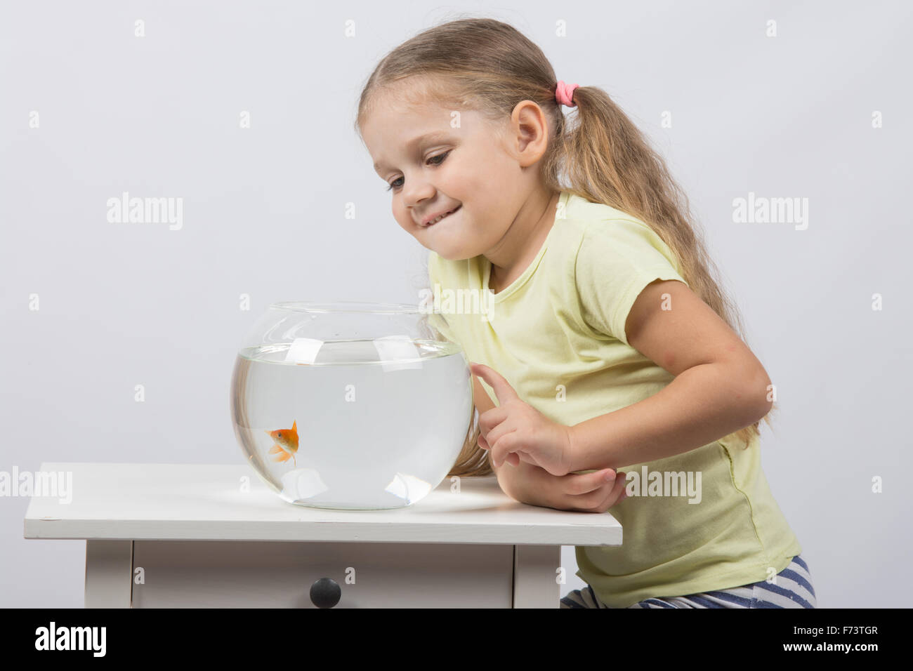 Felice di quattro anni di ragazza seduta al tavolo vicino a fishbowl con pesci rossi Foto Stock