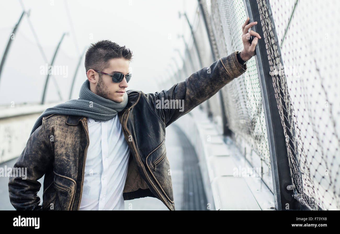 Belli i giovani alla moda uomo in piedi su un marciapiede che indossa una camicia alla moda e sciarpa in un rilassato fiducioso pongono guardando lontano Foto Stock