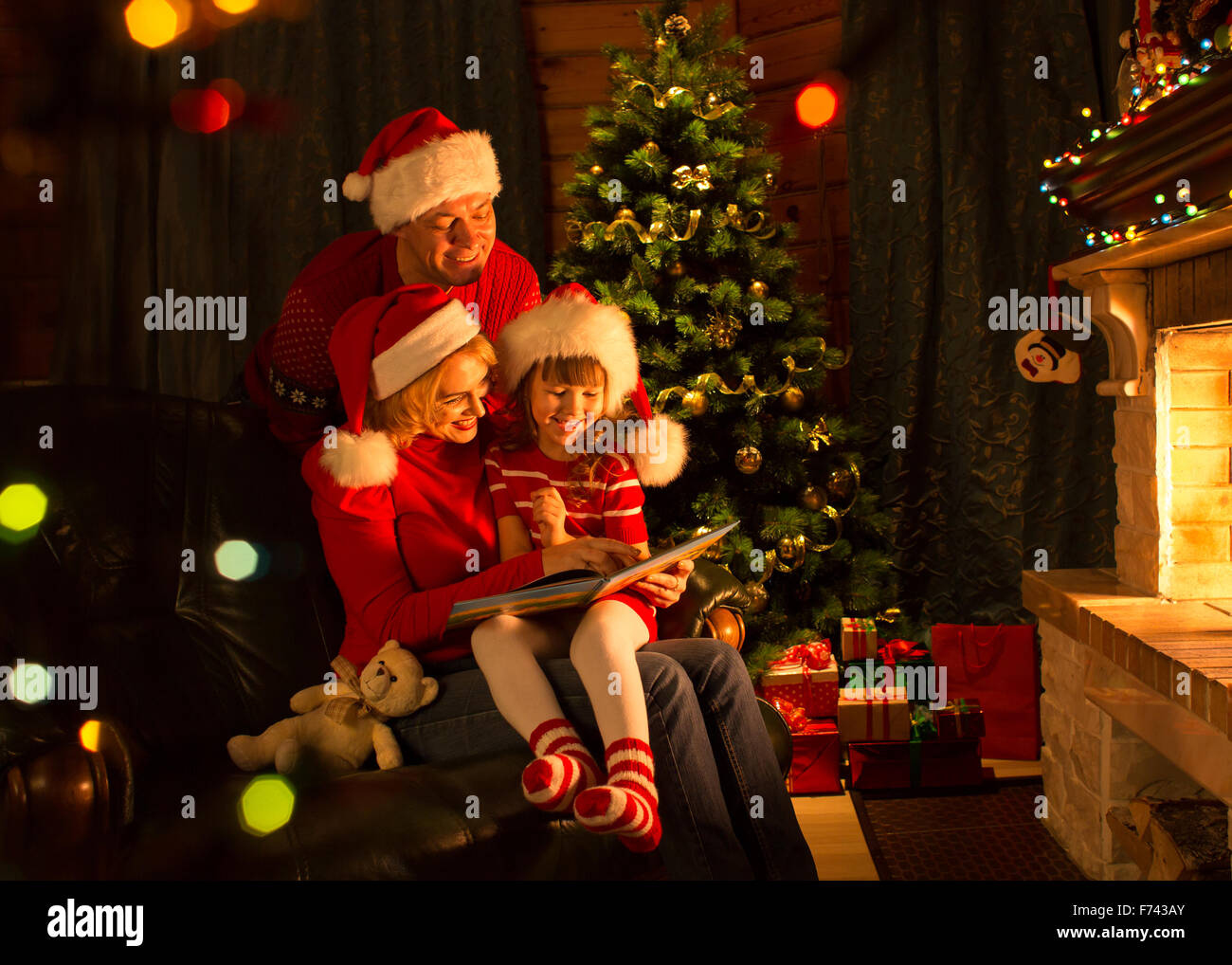 Famiglia leggendo un libro di un albero di Natale in salotto accogliente in inverno Foto Stock