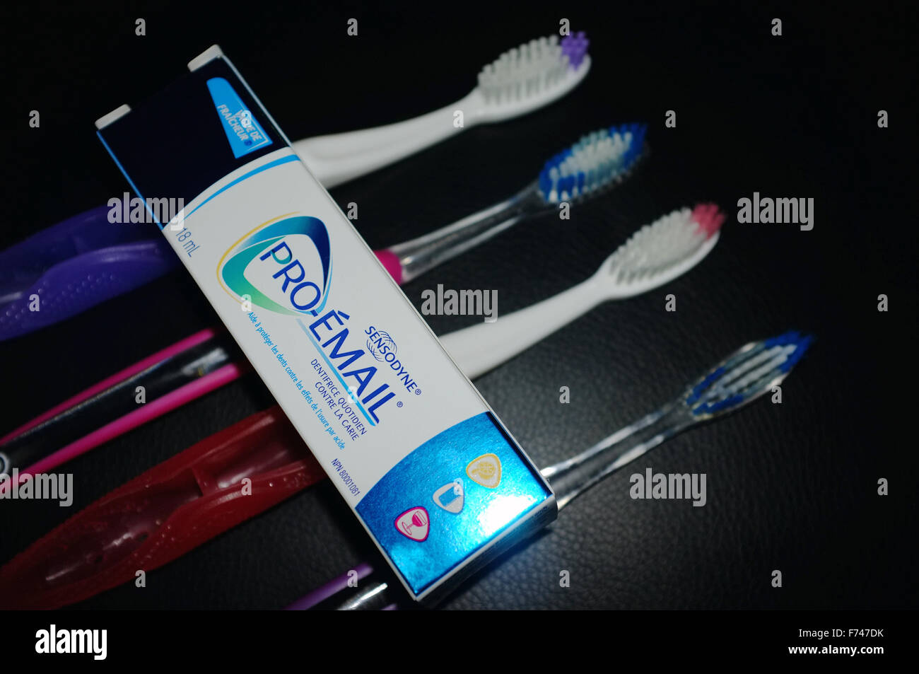 Una fila di quattro spazzolini da denti con un pacchetto di dentifricio fotografati contro uno sfondo nero. Foto Stock