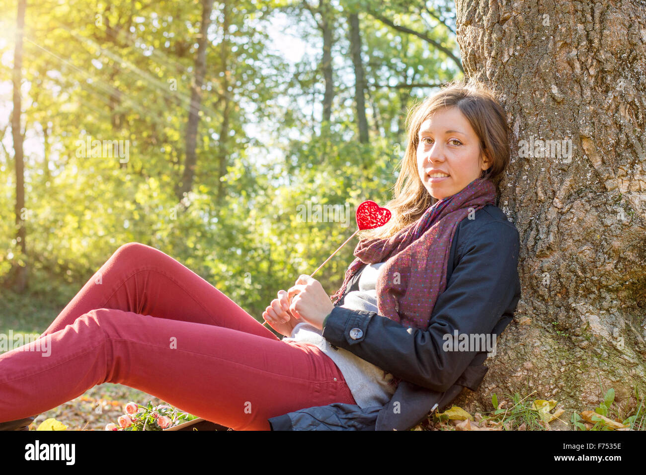 Bellissima ragazza con cuore rosso su un bastone mentre è seduto sull'erba. Relax in una giornata autunnale Foto Stock