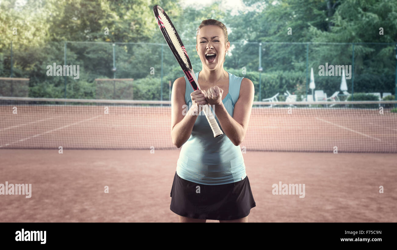 Tre quarti di lunghezza Ritratto di atletica donna bionda Holding Racchetta da Tennis e celebrando con la bocca aperta e la mano gesto su Foto Stock
