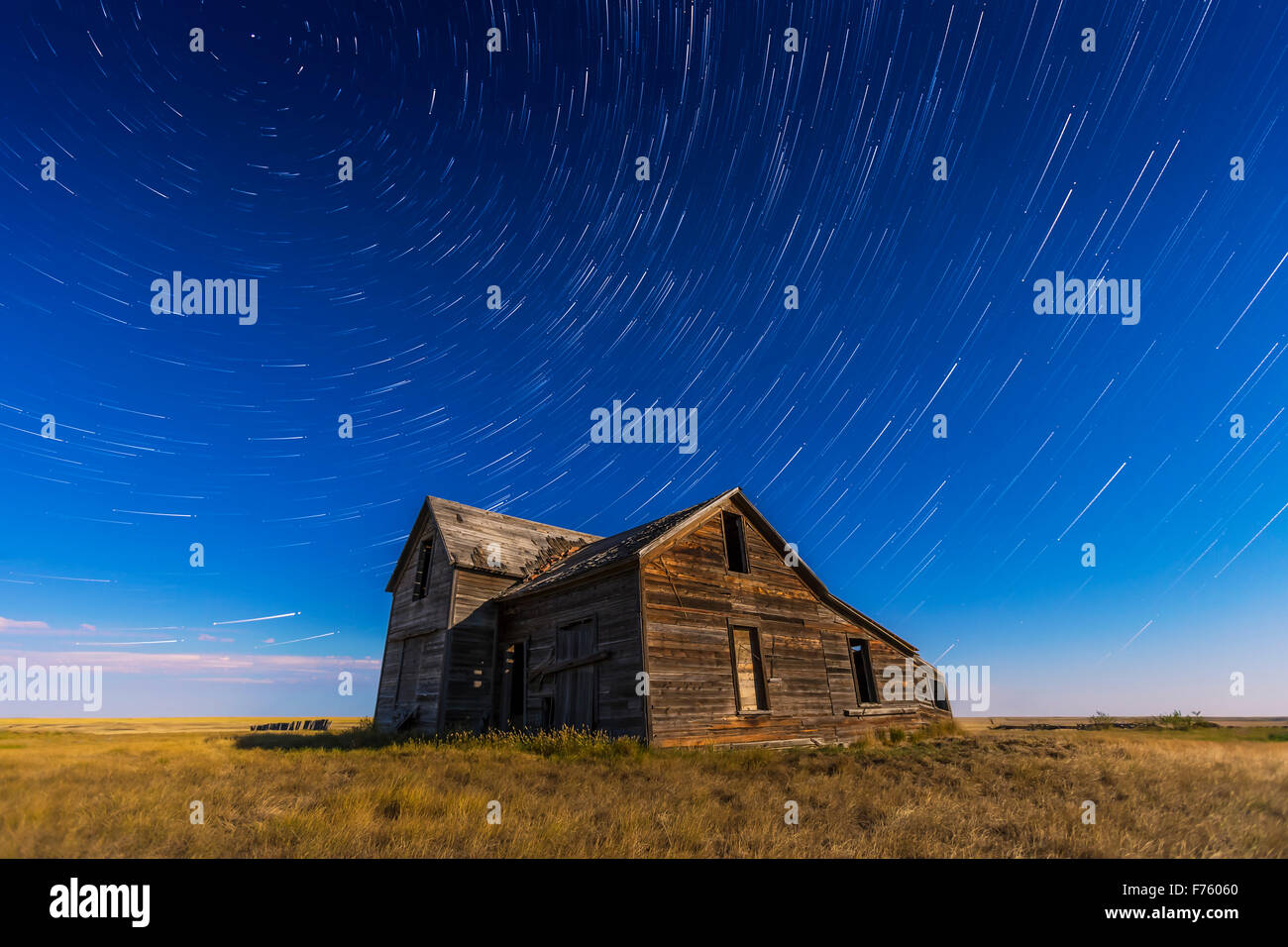 Stella circumpolare sentieri volteggiare al di sopra di un vecchio rustico e casa abbandonata vicino all isola di prua, Alberta, con illuminazione da ne Foto Stock