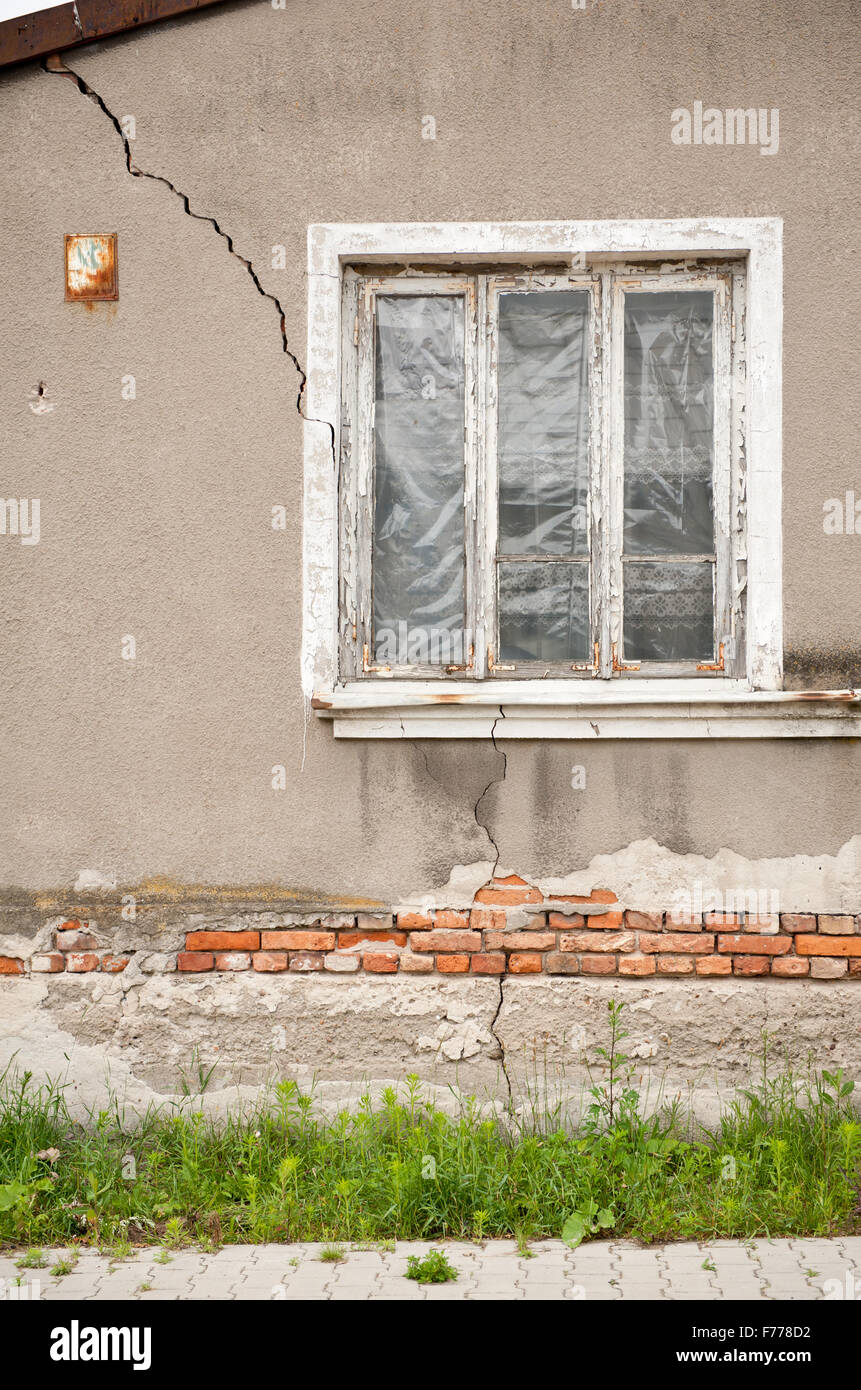 Casa decrepita parete incrinata e fessura, vecchia casa abbandonata con la lamina nella finestra e bocchetta a lancia in tutto il lato, casa danneggiata... Foto Stock