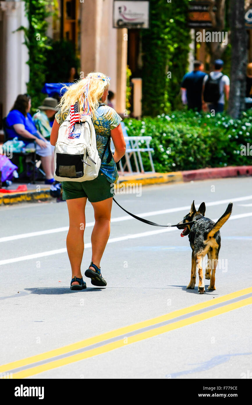 Capelli biondi donna prendendo il suo cane per una passeggiata in mezzo alla strada a Santa Barbara in California il 4 luglio Foto Stock