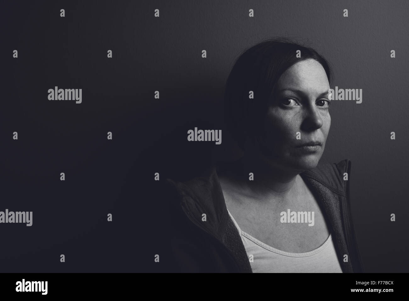 Intensa chiave di basso ritratto di pensieroso triste donna appoggiata su grigio della parete della camera, basso contrasto immagine monocromatica Foto Stock