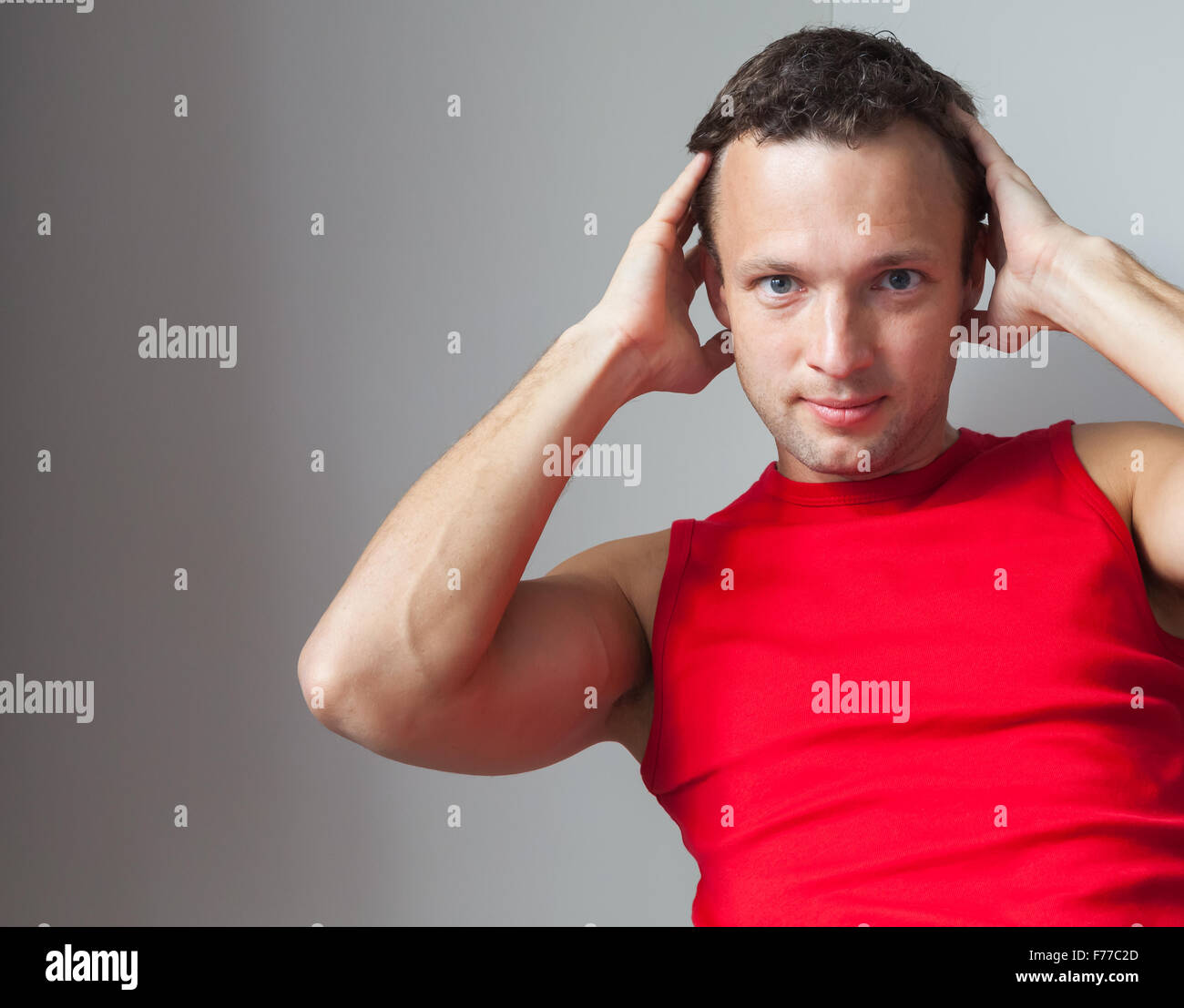 Giovane uomo caucasico in rosso maglia sportiva fa un esercizio sui muscoli addominali Foto Stock