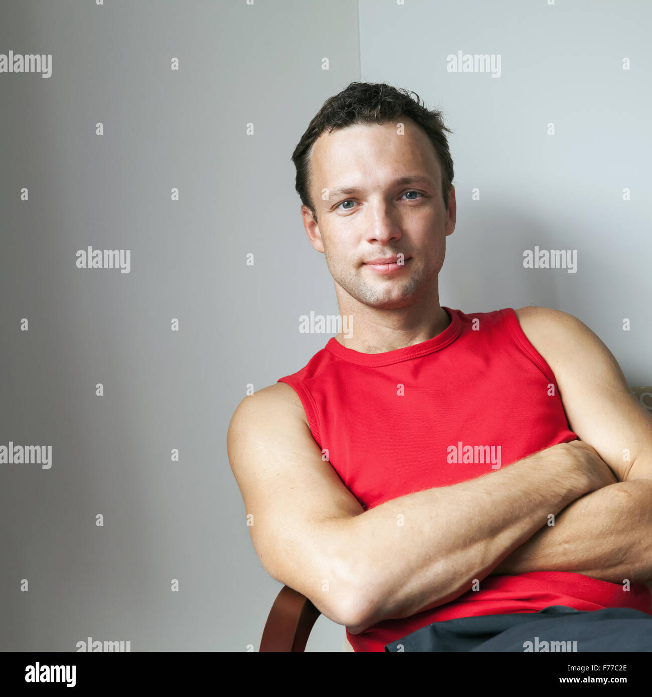 Giovane uomo caucasico in rosso maglia sportiva seduta con bracci incrociati Foto Stock