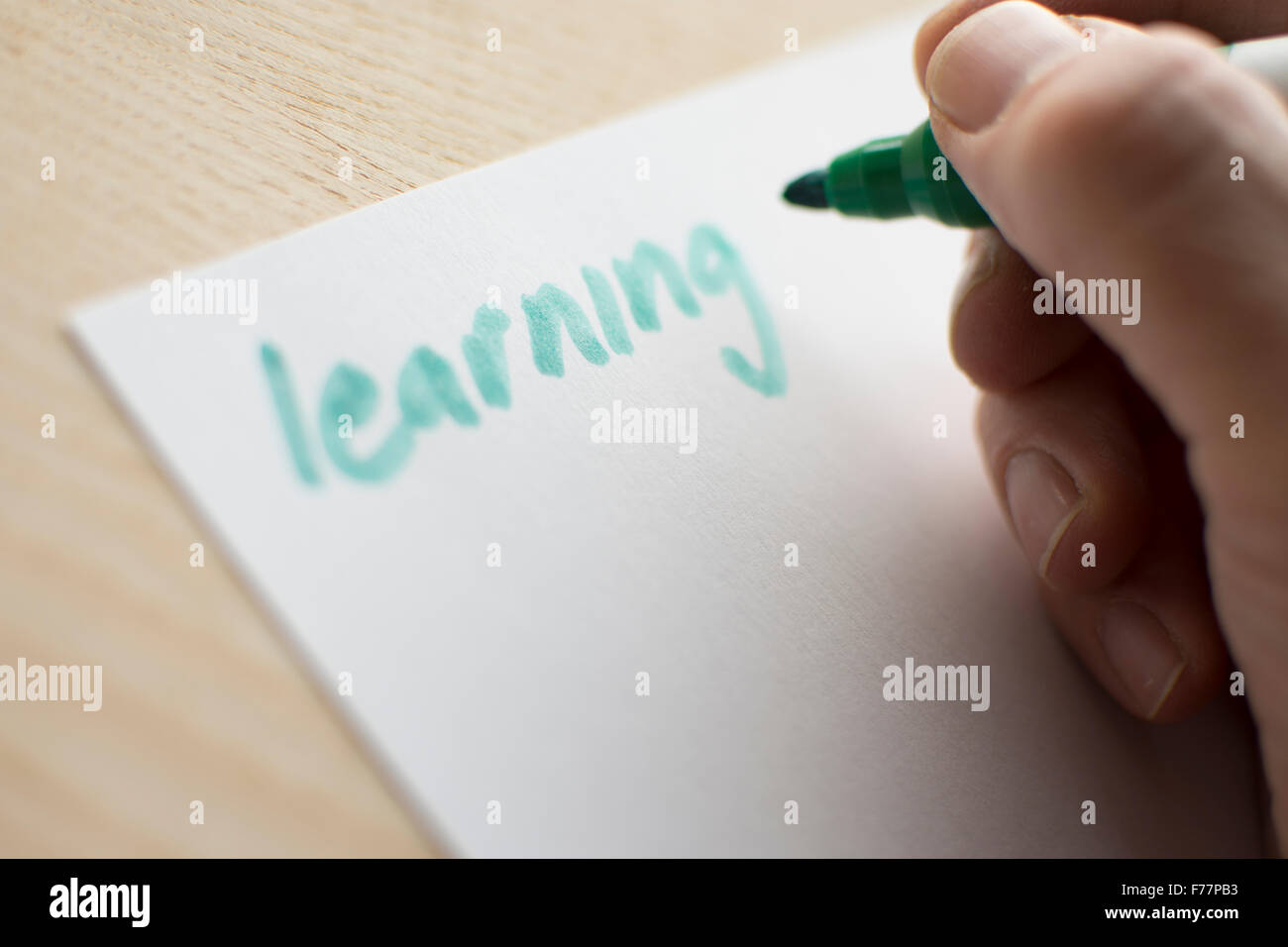 Persona scrivendo la parola 'apprendimento' in verde penna su carta bianca steso su una tavola di legno o da tavolo. Foto Stock
