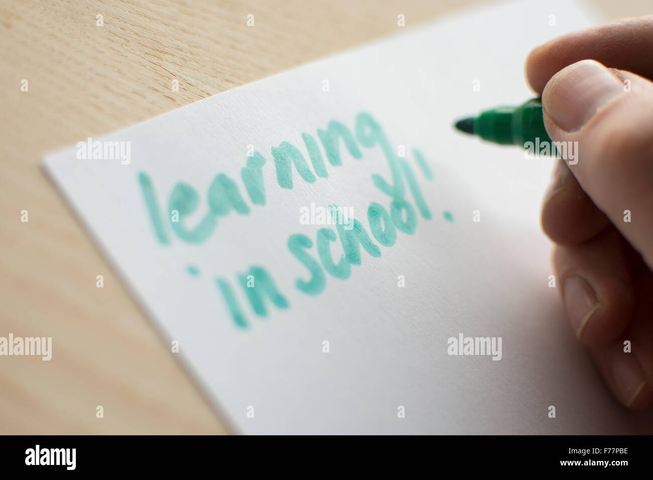 Persona scrivendo la parola 'apprendimento' in verde penna su carta bianca steso su una tavola di legno o da tavolo. Foto Stock