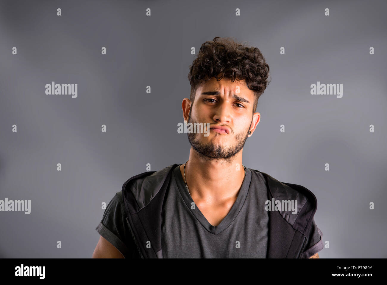 Bello duro giovane uomo in scuro incappucciati t-shirt su sfondo scuro, guardando la fotocamera Foto Stock