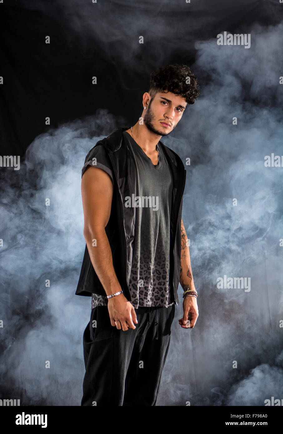 Bello duro giovane uomo in scuro incappucciati t-shirt su sfondo scuro, guardando la fotocamera Foto Stock