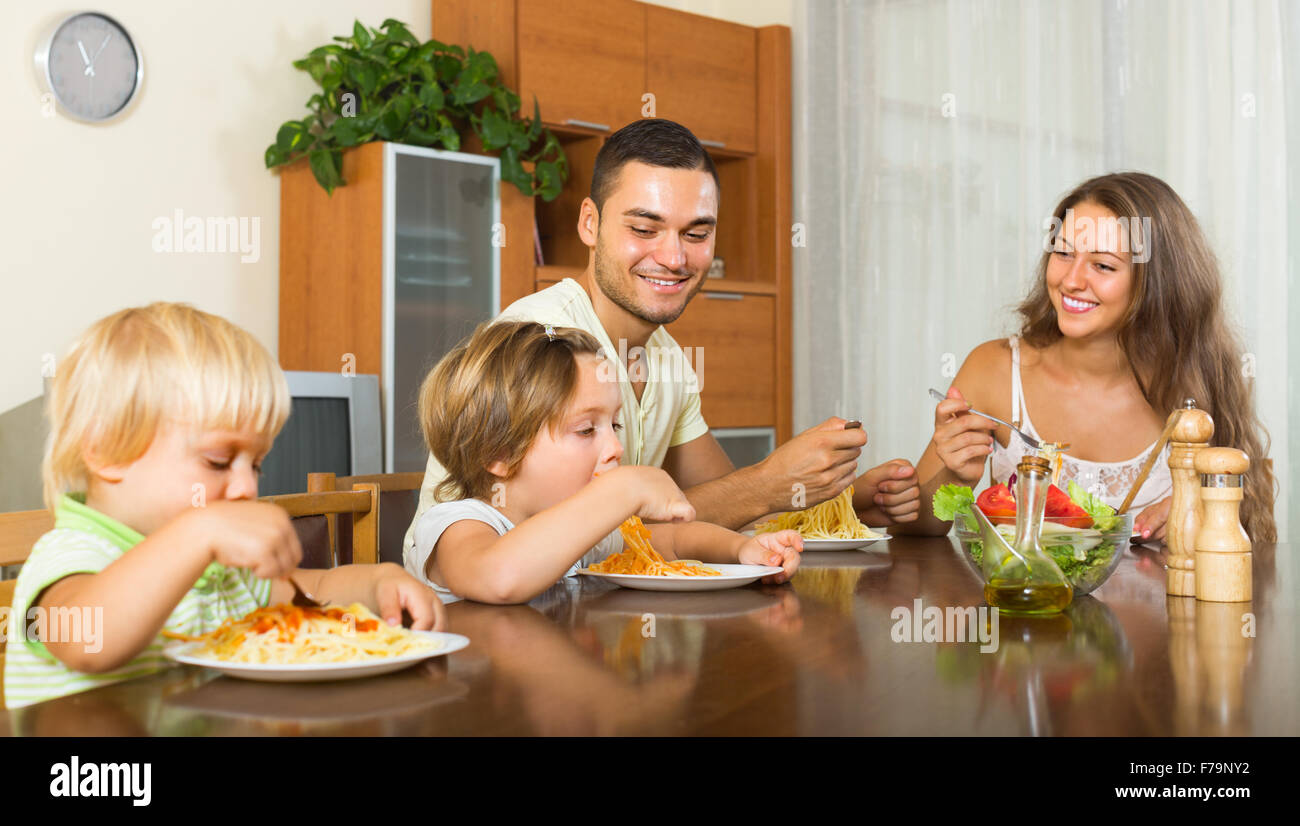 Giovane famiglia sorridente di quattro mangiare spaghetti a casa interni. Focus sull'uomo Foto Stock