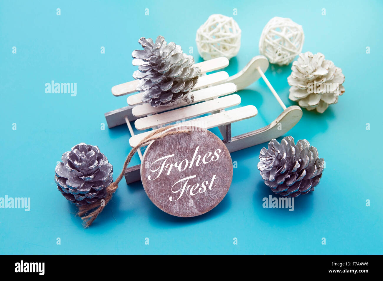 I tedeschi 'Frohes Fest' (Merry Christmas) sul tag di legno con toy sleigh e pigne nelle quali Foto Stock