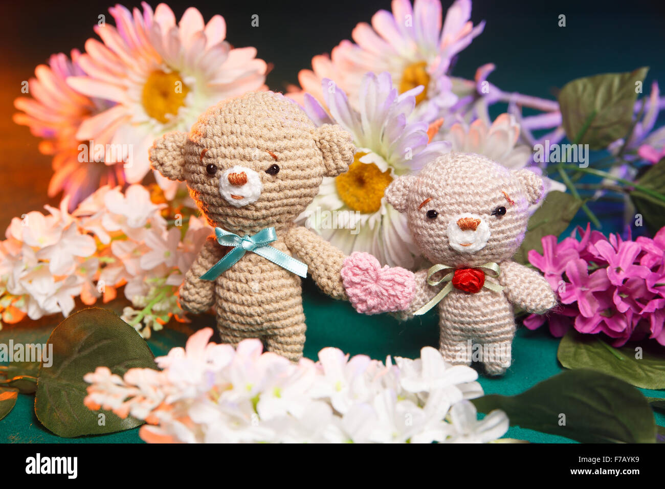 Concetto: amore, relazione. Coppia di orsi in maglia tenendo le mani con fiori sullo sfondo Foto Stock