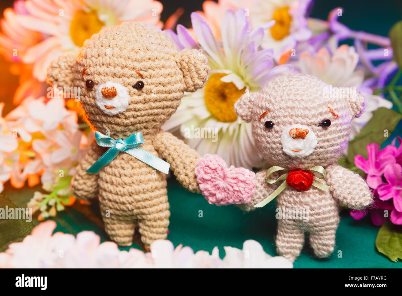 Concetto: amore, relazione. Coppia di orsi in maglia tenendo le mani con fiori sullo sfondo Foto Stock