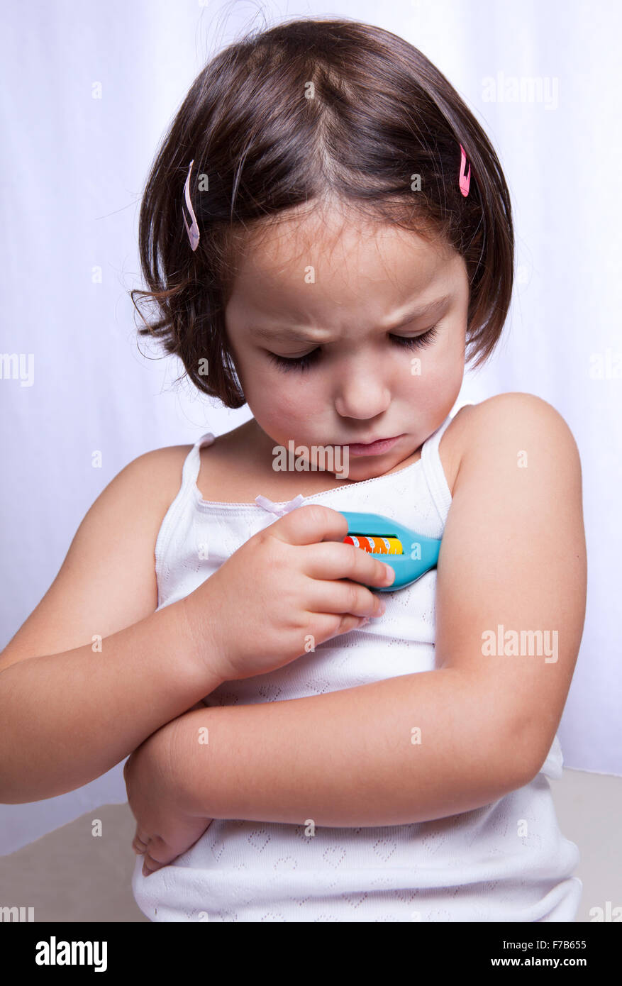 Carino bambina riproduzione medico con termometro giocattolo. Isolato su sfondo bianco Foto Stock