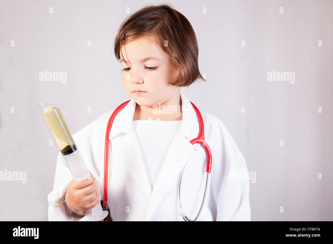 Bambina vestito come un medico in possesso di una enorme siringa. Isolato su sfondo bianco Foto Stock