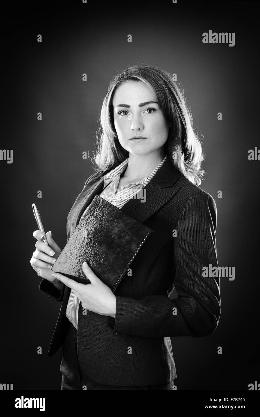 Ritratto di una donna d'affari shot in studio su sfondo grigio in possesso di un notebook e penna Foto Stock