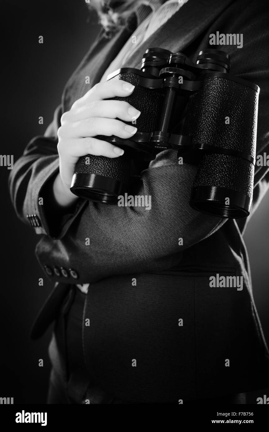 Immagine ravvicinata di business donna tenendo il binocolo shot in studio su sfondo grigio Foto Stock