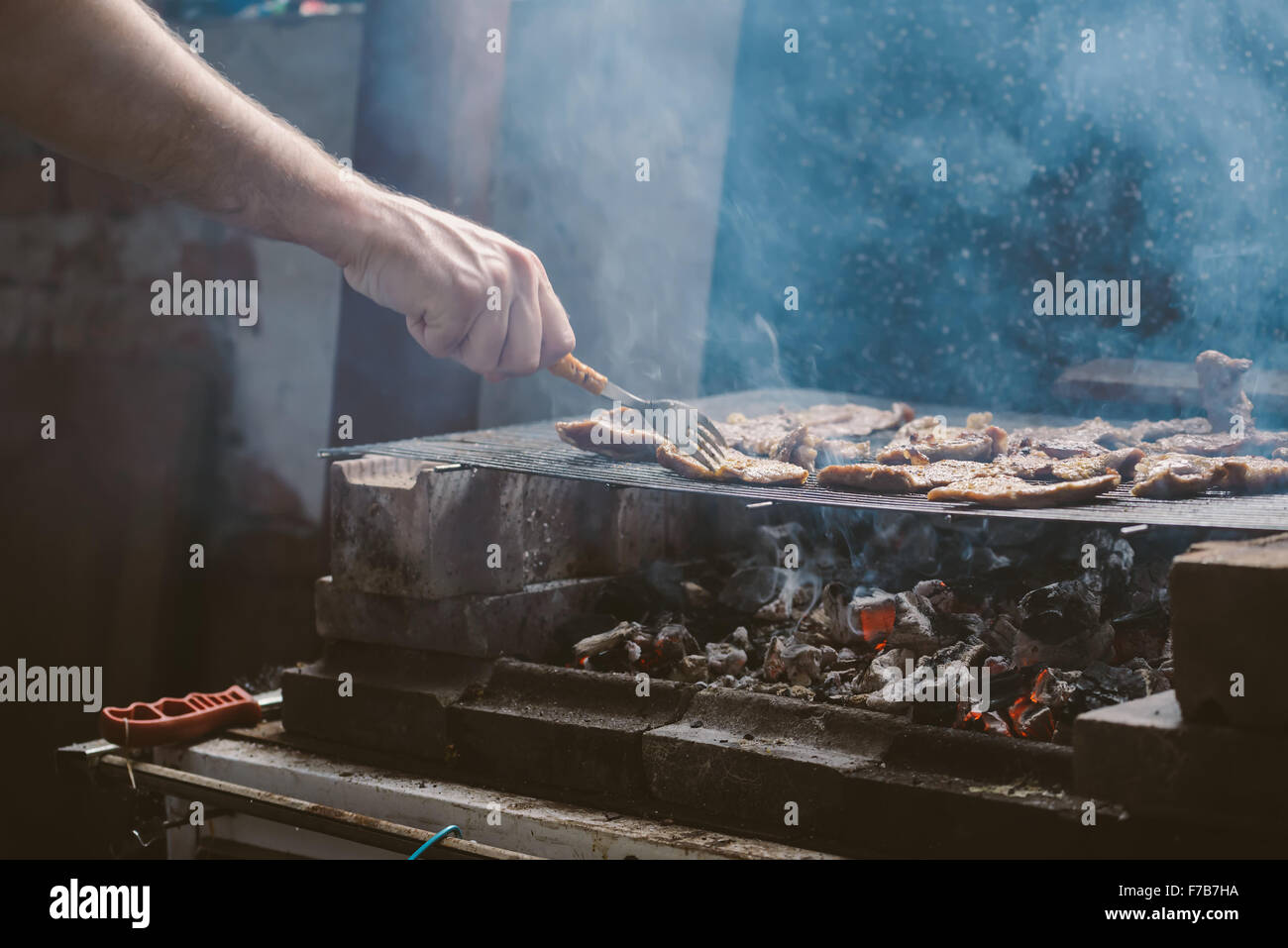 L uomo per grigliare carne di maiale braciole sul barbecue, luce naturale, dai toni retrò, messa a fuoco selettiva con profondità di campo ridotta. Foto Stock