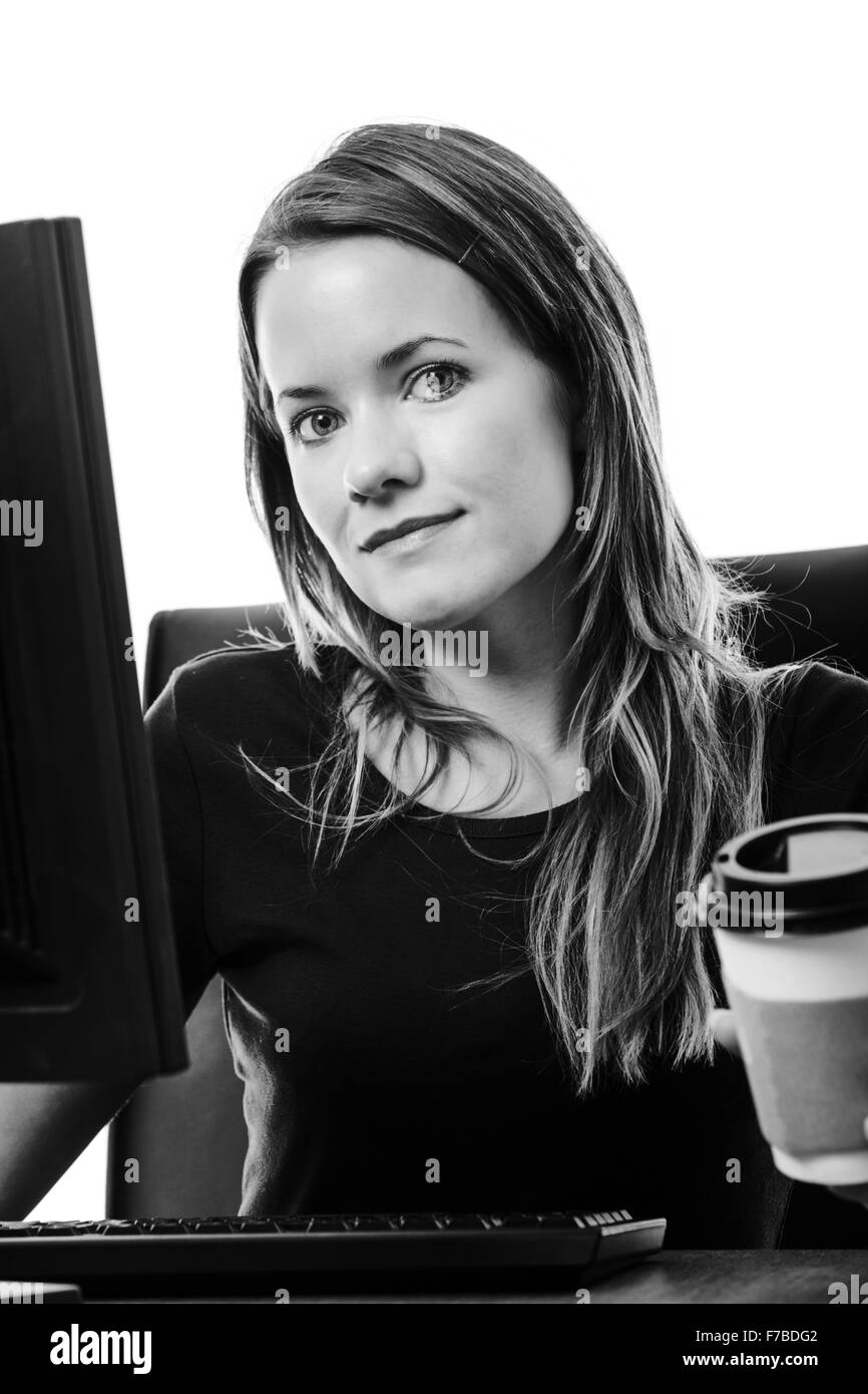 Donna che lavorano alla sua scrivania sul computer di bere il caffè Foto Stock