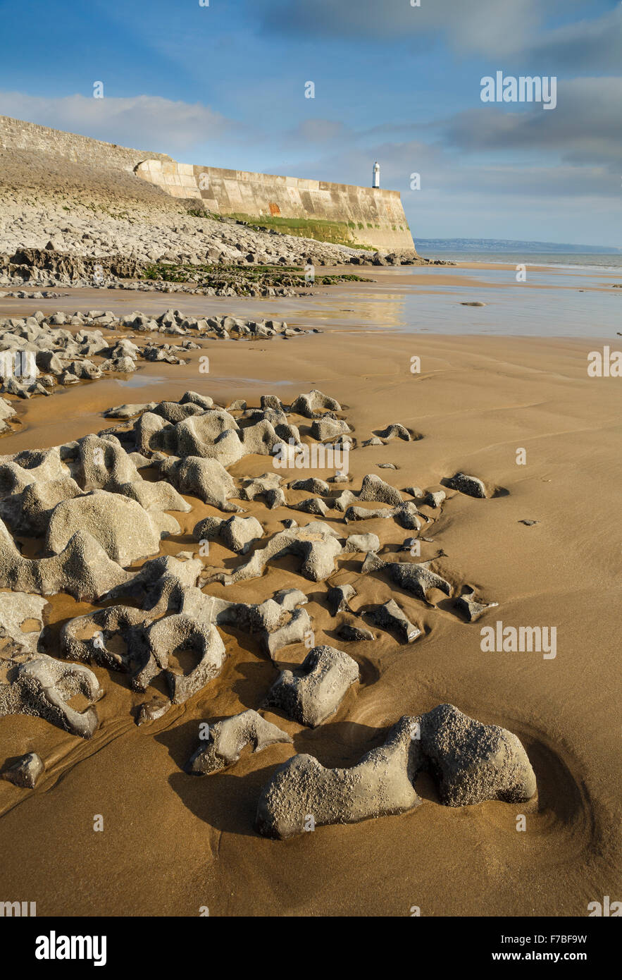 Le splendide formazioni rocciose a bassa marea a Porthcawl, Vale of Glamorgan, Galles. Il tramonto è l'illuminazione fino al faro e break Foto Stock