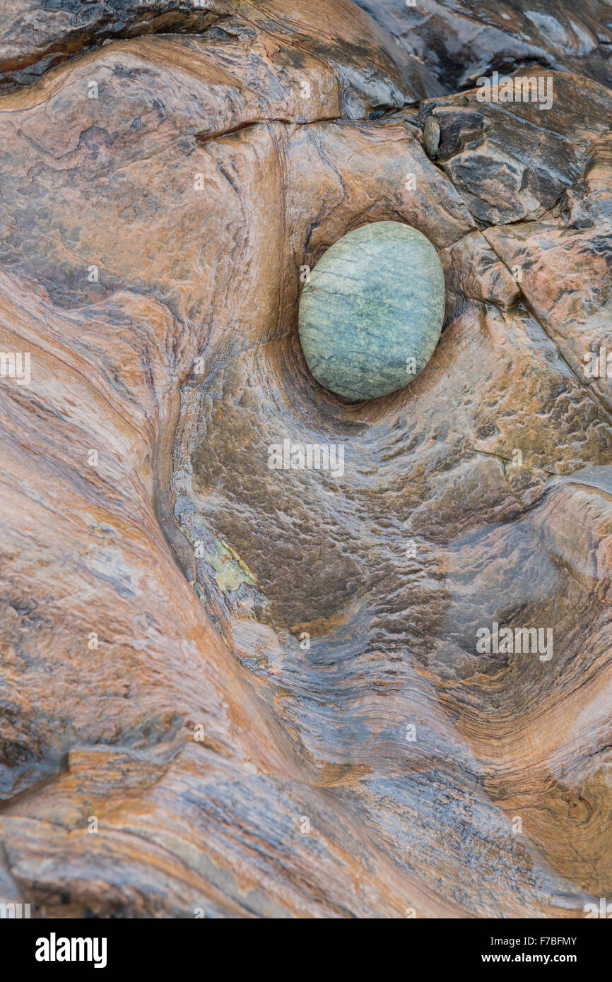 Un verde ciottolo si siede in un foro nella roccia di colore arancione. Foto Stock