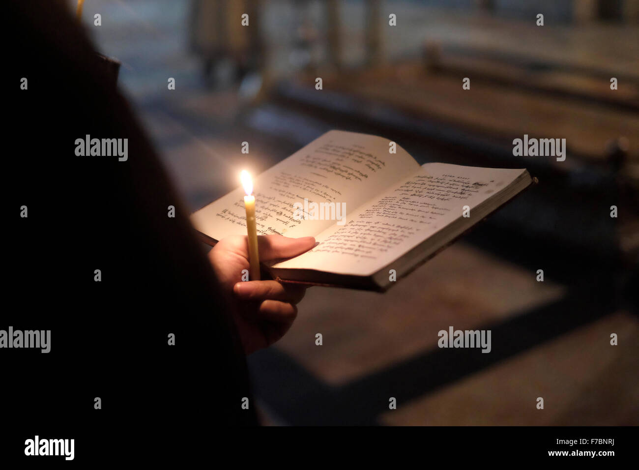 Chiesa armena apostolica chierico detiene una candela su un aperto hymnal prenota nel della chiesa del Santo Sepolcro nella città vecchia di Gerusalemme Est Israele Foto Stock