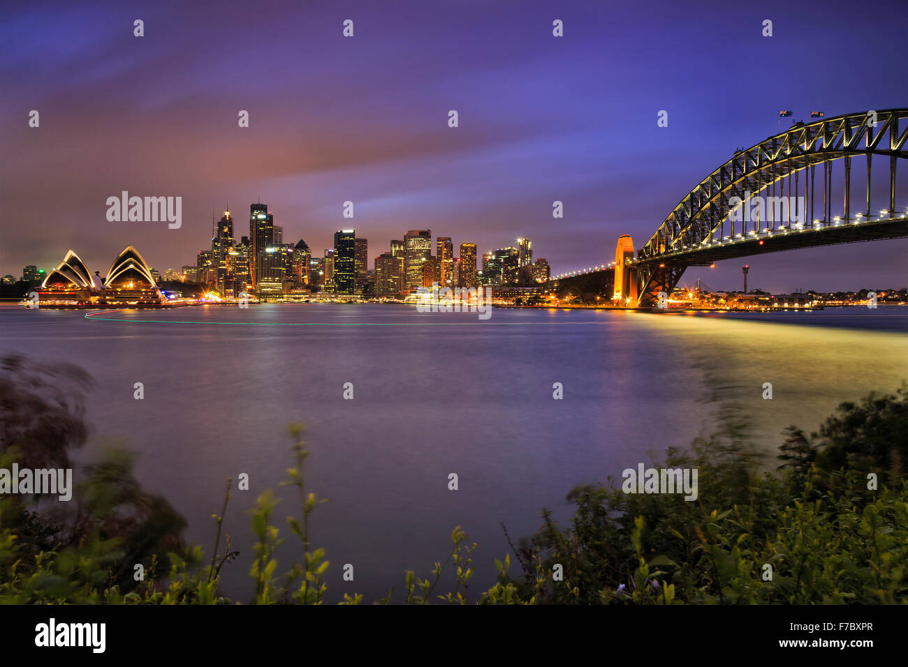 I punti di riferimento della città di Sydney CDB attraverso il porto con arco del ponte, grattacieli e casa al tramonto con illuminazione completa Foto Stock