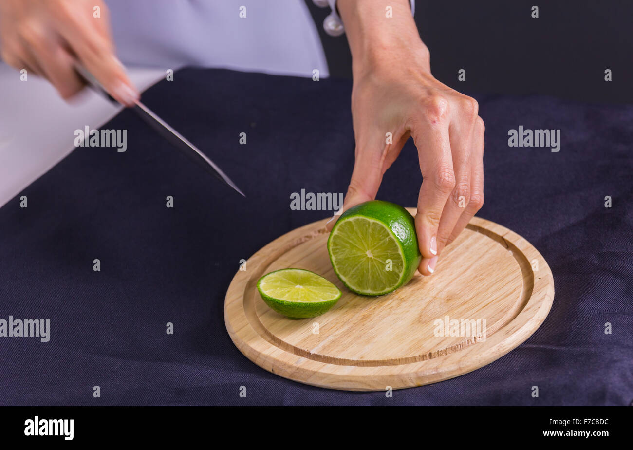 Fresco e acidulo verde lime o limone, tagliata a metà con il coltello sul tagliere Foto Stock