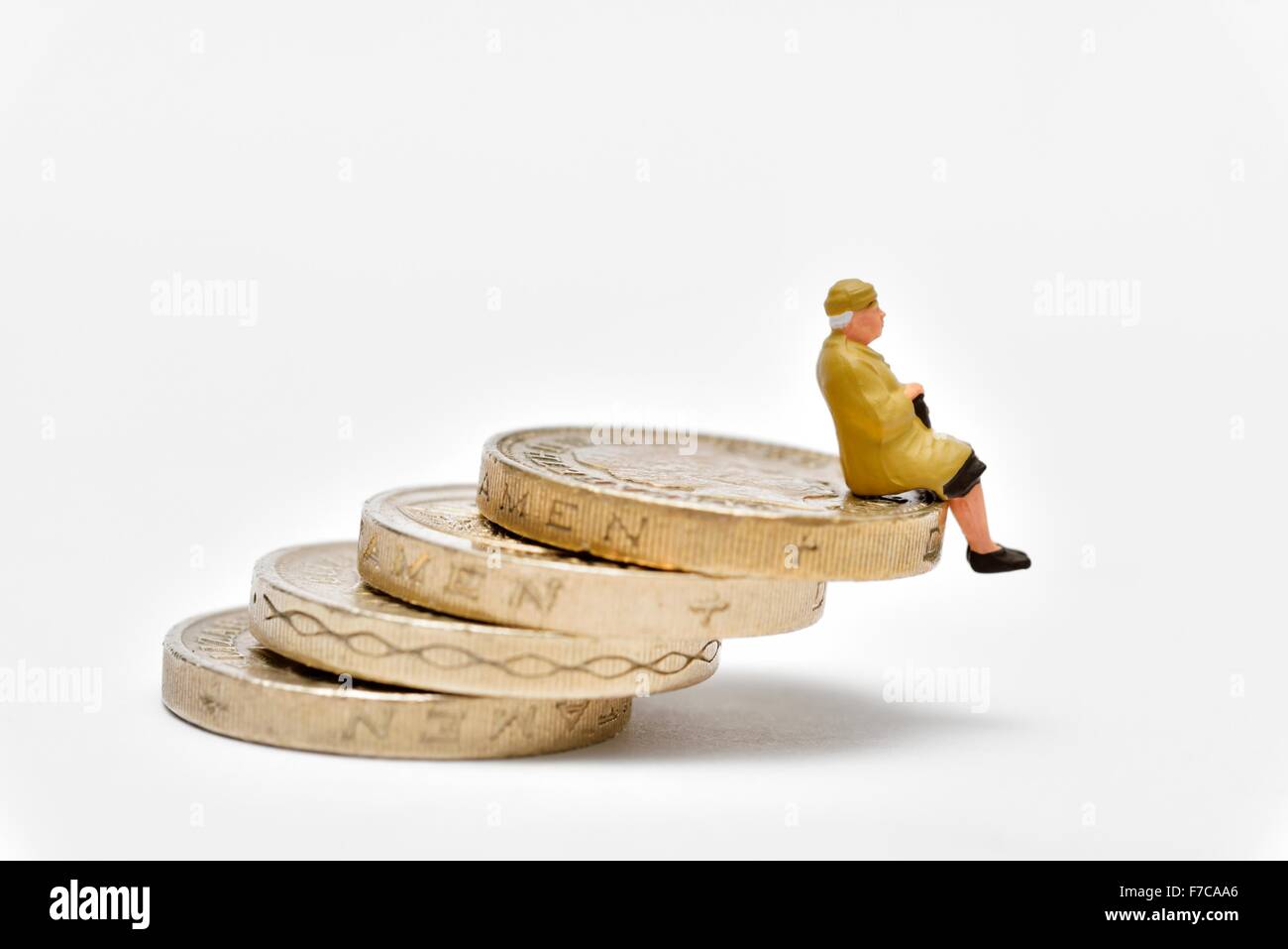 Femmina miniaturizzati pensionato seduto bilanciato su una pila di libbra di monete Foto Stock
