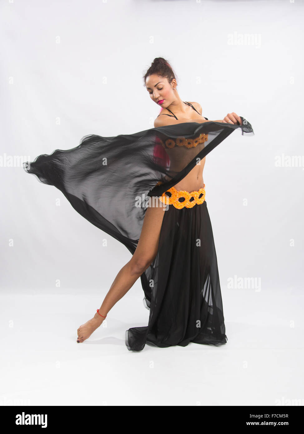 Ragazza giovane mulatto dancing in un lungo nero candido abito aperto, è isolato su uno sfondo luminoso Foto Stock