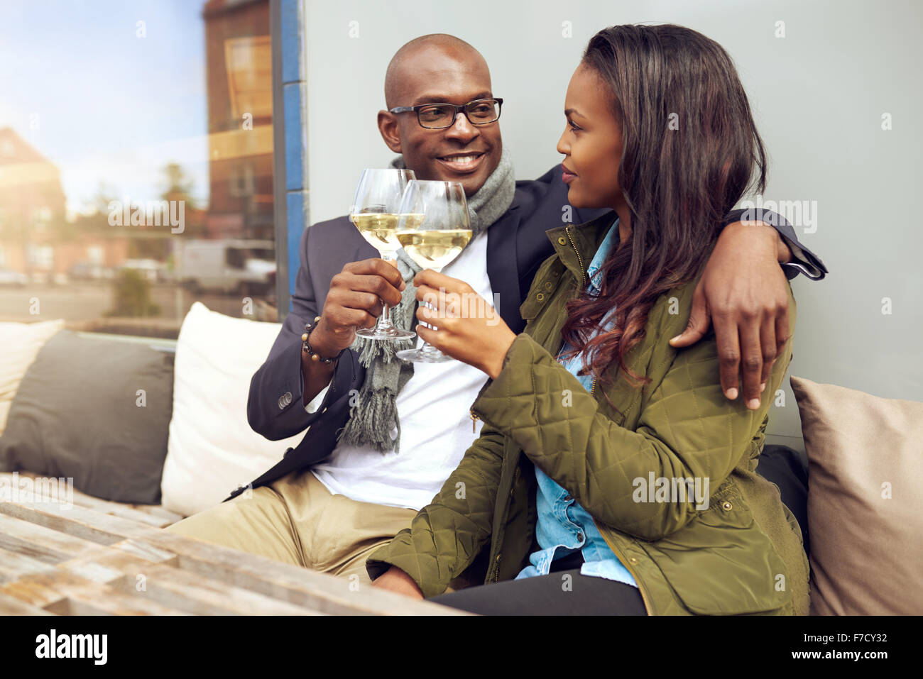 Felice giovane africano coppia americana godendo di un romantico un bicchiere di vino bianco come si siedono a braccetto in un ristorante Foto Stock