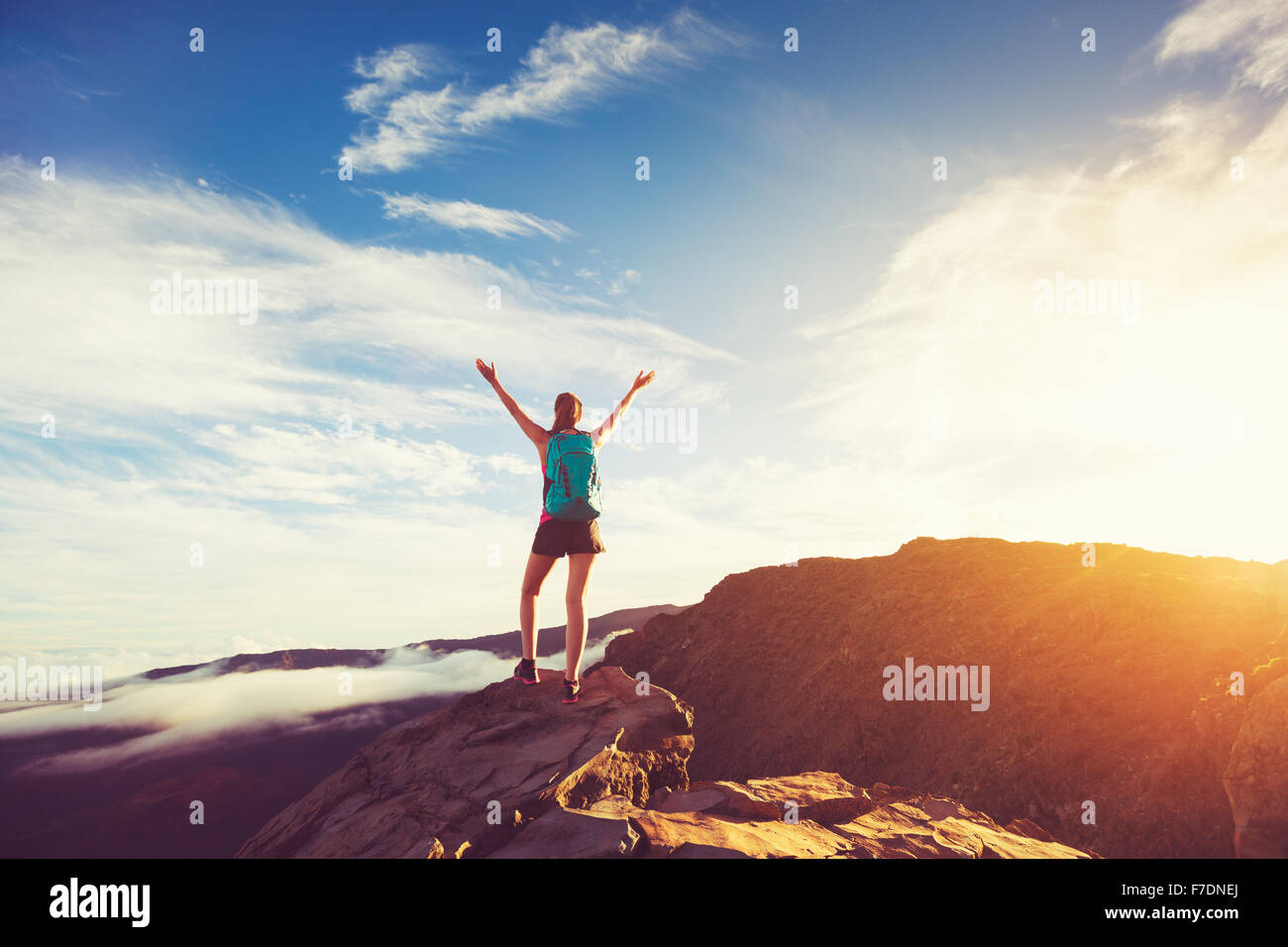 Felice giovane donna escursionista con le braccia aperte sollevate al tramonto sul picco di montagna Foto Stock