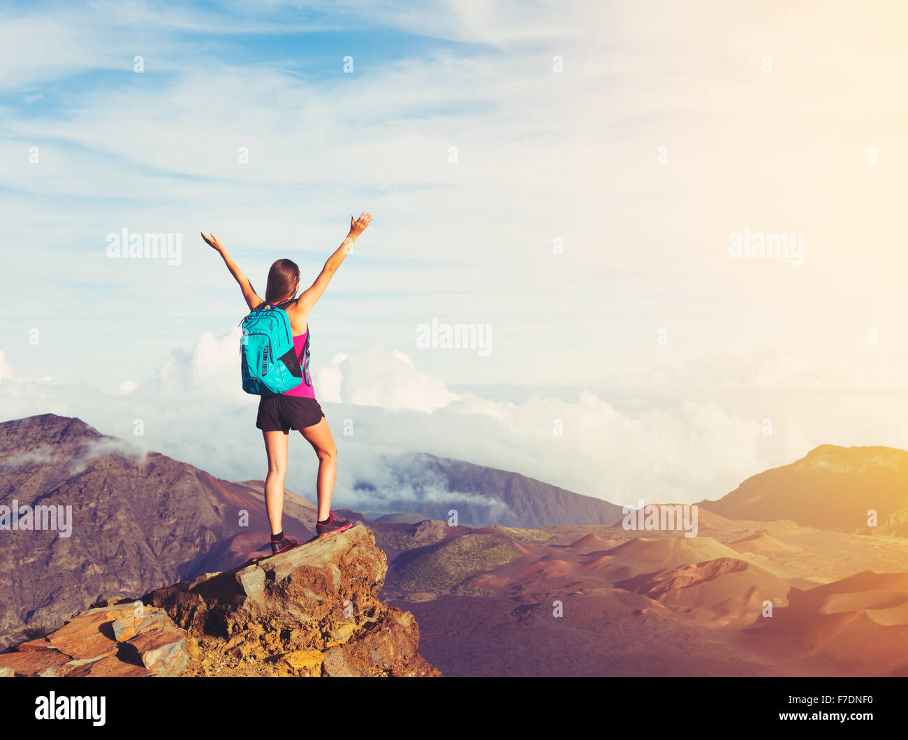 Felice giovane donna escursionista con le braccia aperte sollevate al tramonto sul picco di montagna Foto Stock