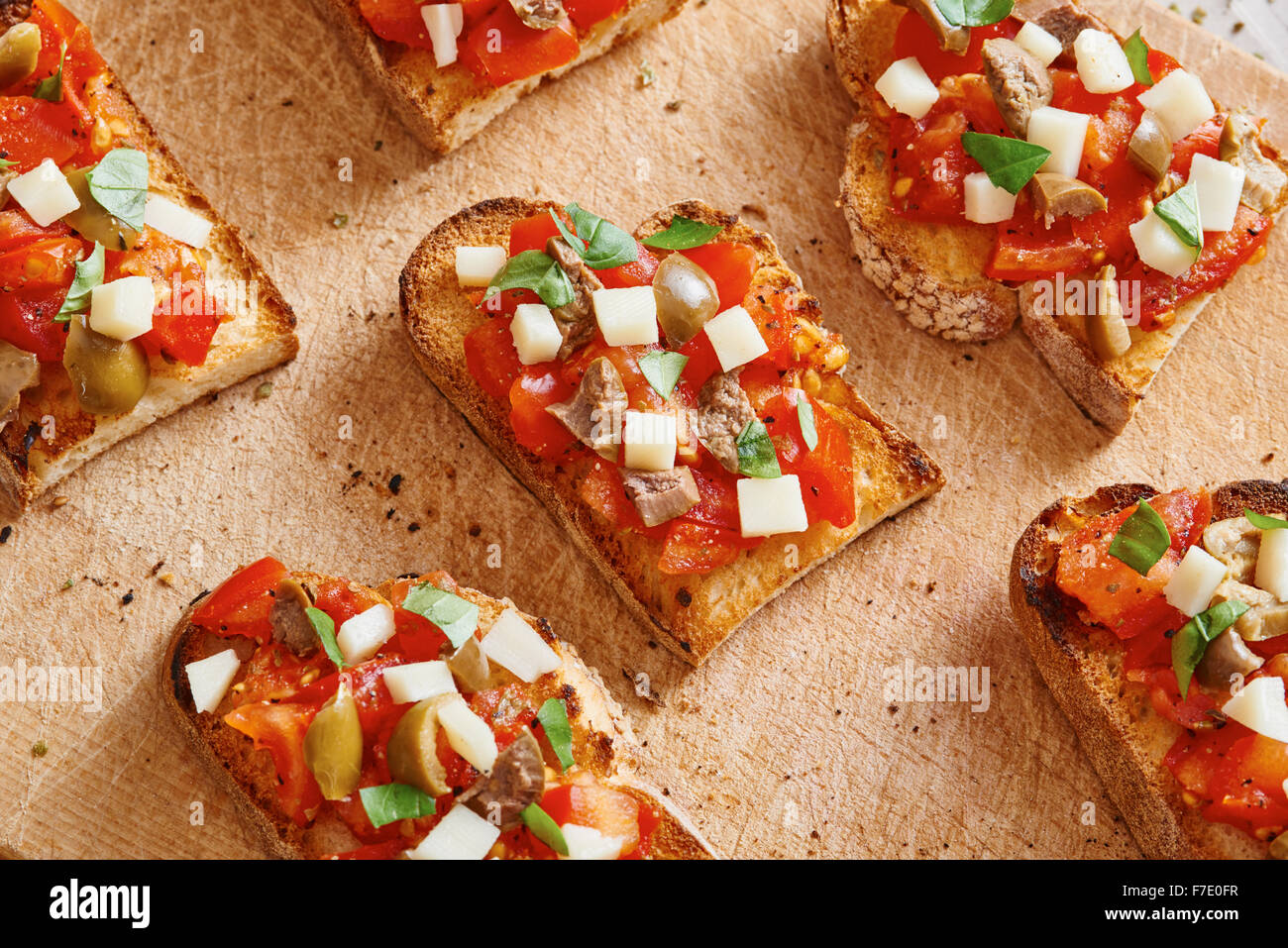 La bruschetta al pomodoro, formaggio, olive e l'aglio sul tagliere e tavolo in legno circondato da pomodoro e aglio Foto Stock