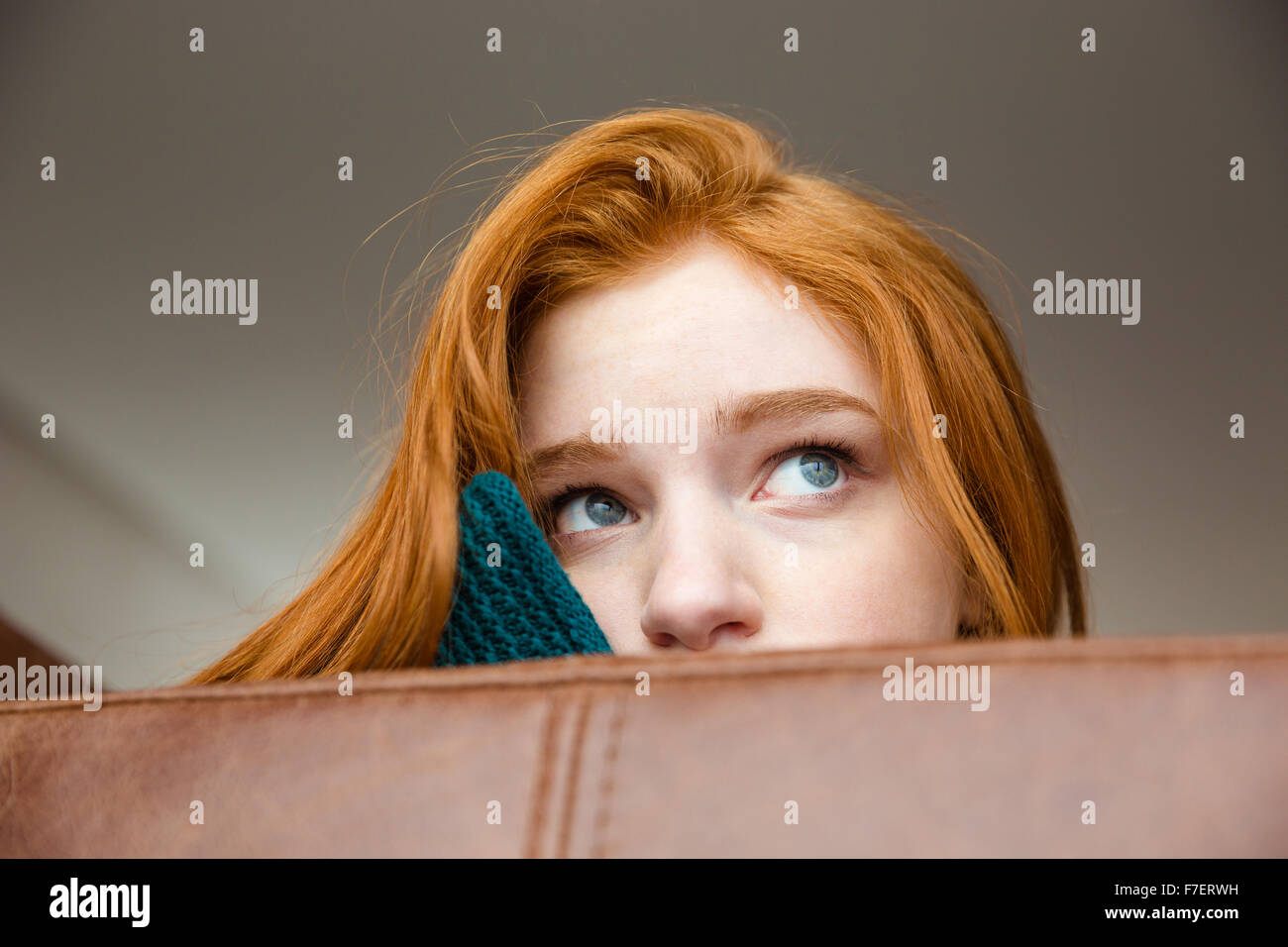 Insicuro timido redhead girl sbirciando su divani in pelle marrone e guardando lontano Foto Stock