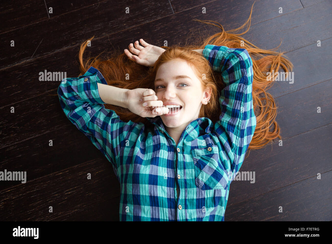 Vista superiore della gioiosa attraente redhead girl in plaid shirt sdraiato sul pavimento in legno Foto Stock