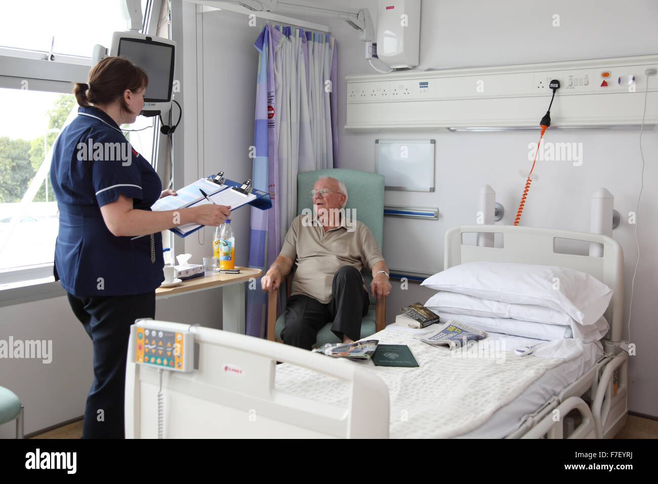 Un'infermiera parla con un paziente anziano in un moderno reparto ospedaliero britannico. (Nomi e dati medici rimossi per l'anonimato) Foto Stock
