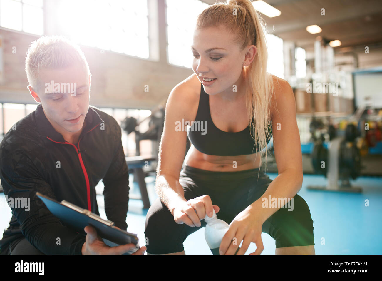 Inquadratura di un personal trainer aiutando giovane donna con il suo piano di fitness. Palestra il trainer e il membro a discutere di un programma di esercizi su clipboa Foto Stock