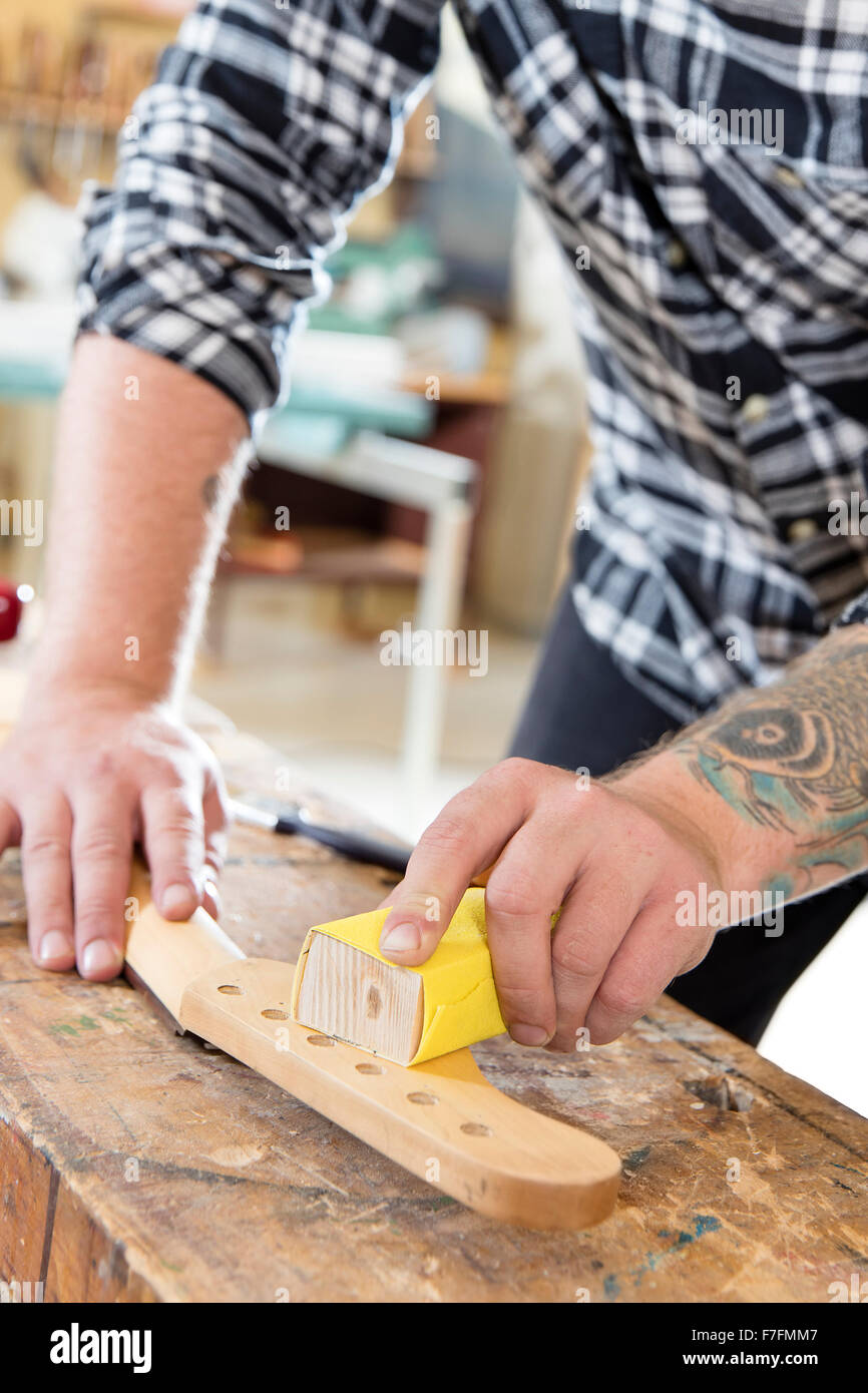 Carpenter la levigazione di un collo per chitarra in legno in officina Foto Stock