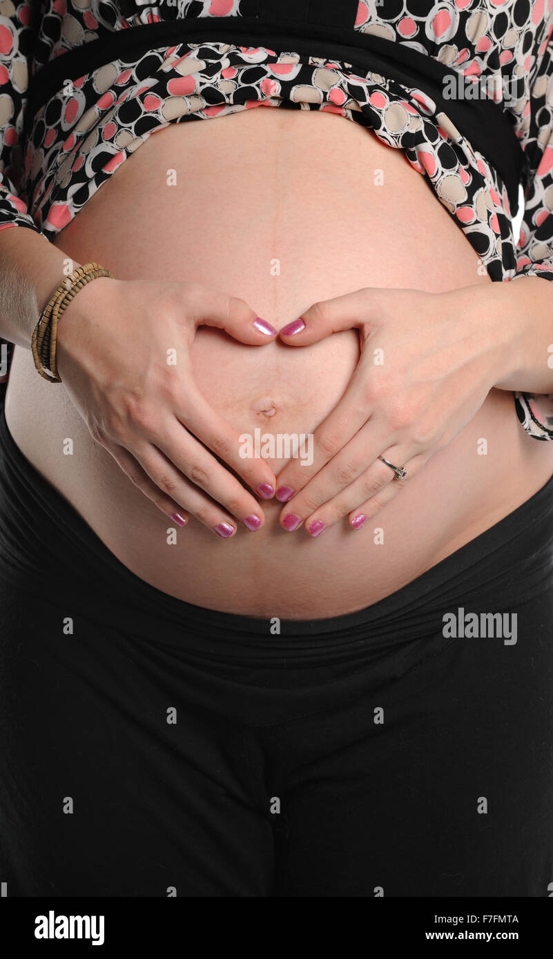 Donna incinta con le mani in mano messa a forma di cuore sulla stomaco Foto Stock