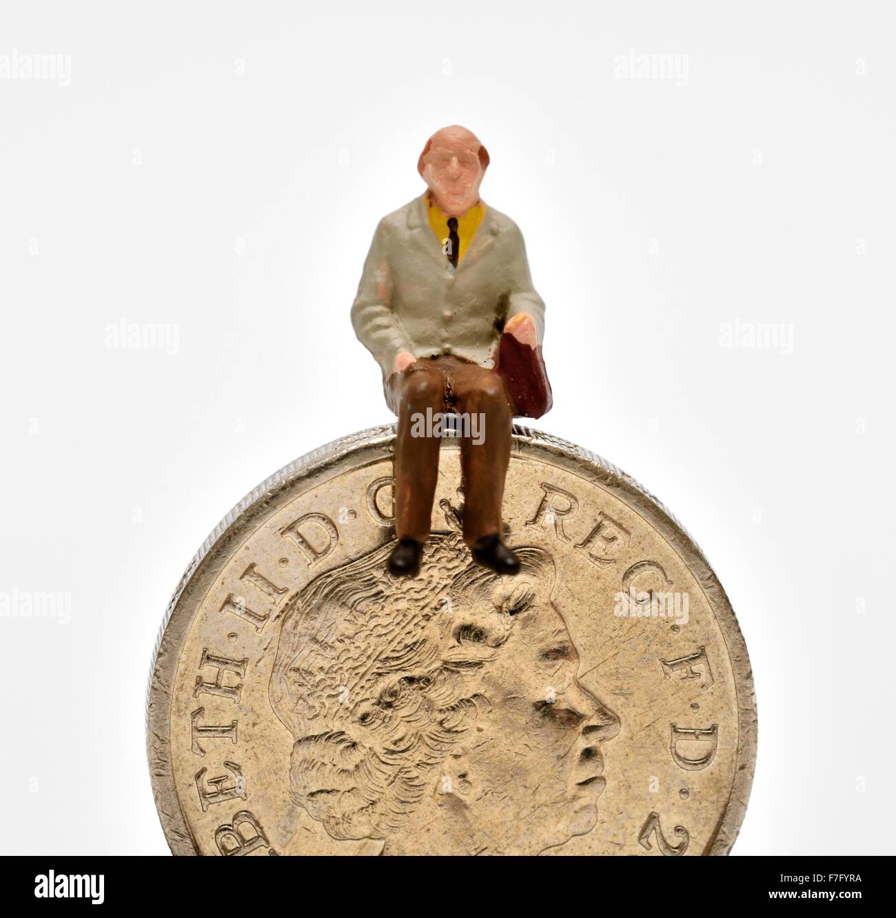 Maschio in miniatura pensionato seduto su una libbra di moneta Foto Stock