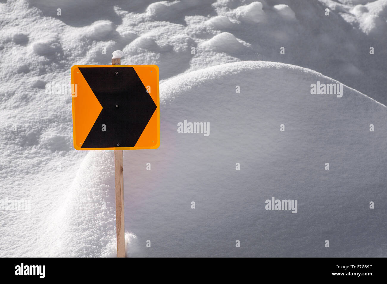 Un arancione e nero trail segno del puntatore bloccato in un cumulo di neve. Foto Stock